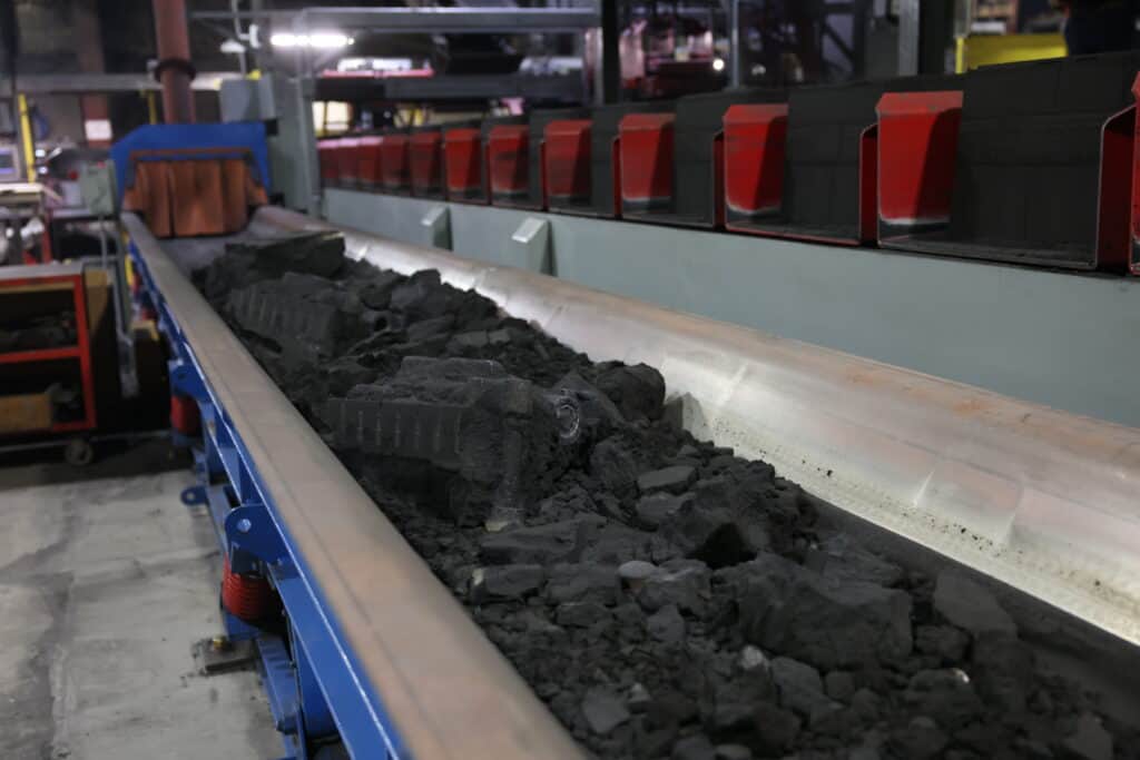 Green sand castings spread out on a conveyor.